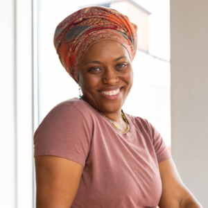 A Black woman wearing a colorful hair scarf smiles