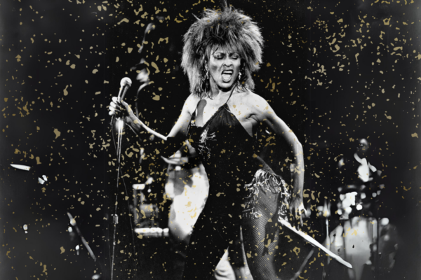 A black & white photograph of Tina Turner onstage, wearing a black dress. She is holding her microphone stand and singing passionately, looking off toward the side. Instruments are barely visible in the background, and there is a vintage-looking golden confetti-esque treatment over the image.