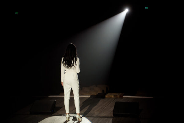 Back view of a singer with microphone singing popular song on stage in white lights.