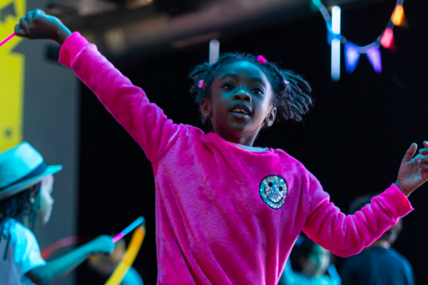 Young black girl with braids dancing in a pink sweater