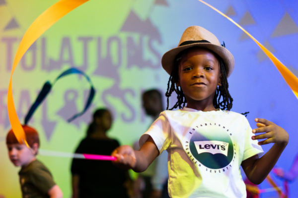 Young Black boy in fedora and t shirt with Levi's log waves a yellow ribbon